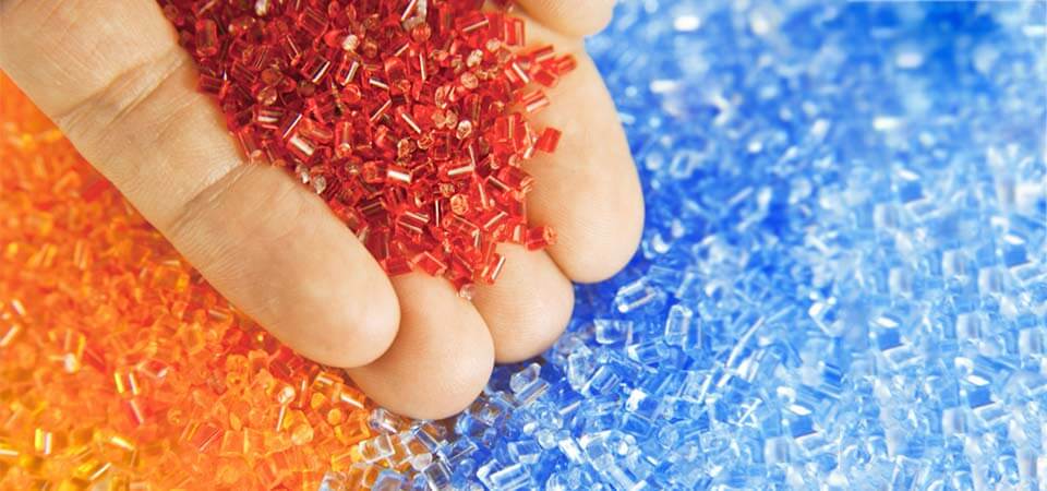 Eine Hand hält rote Granulate vor weiteren orangenen und blauen Granulaten.